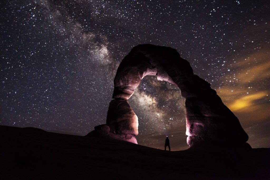 person standing under a rock formation on a starry night milky way